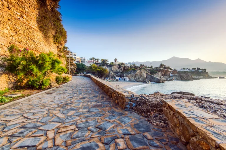 A stone path along the sea by a small cove in Nerja, with the mountains behind